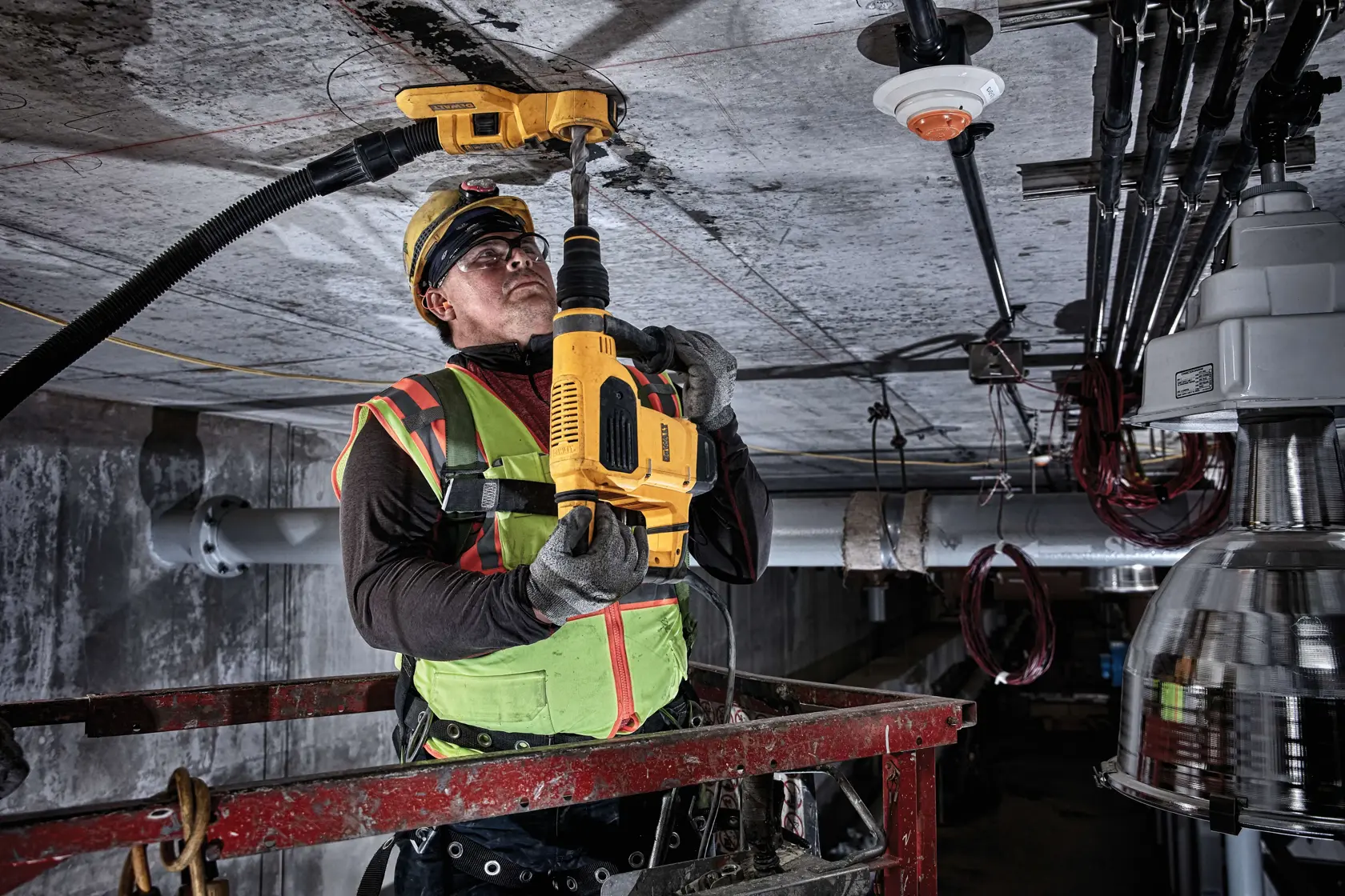 Trabajador taladra el techo con herramienta DEWALT, usando chaleco de alta visibilidad y equipo de seguridad.
