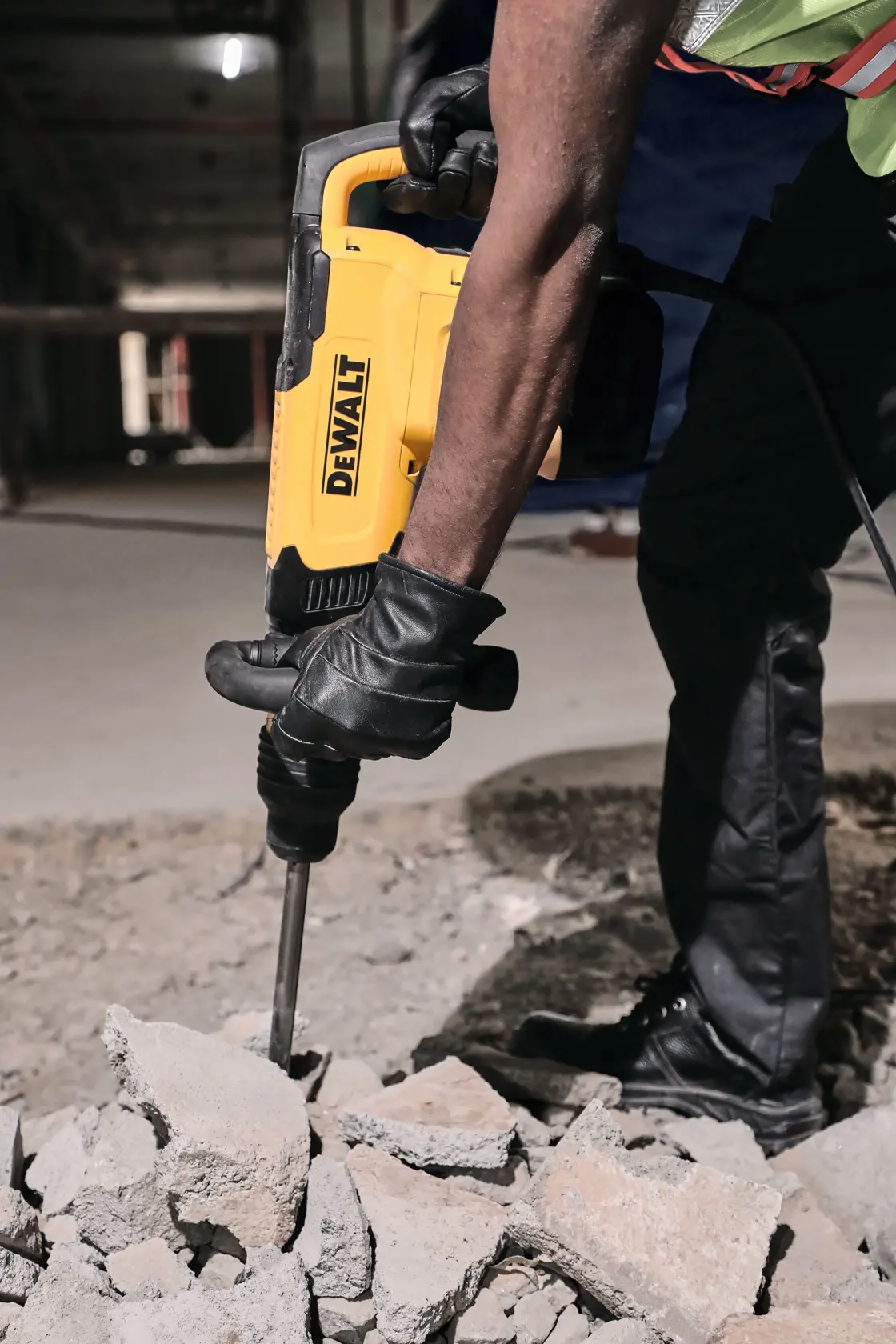 Primer plano de una persona con guantes utilizando un martillo demoledor amarillo DEWALT para romper escombros de concreto en un sitio de construcción.