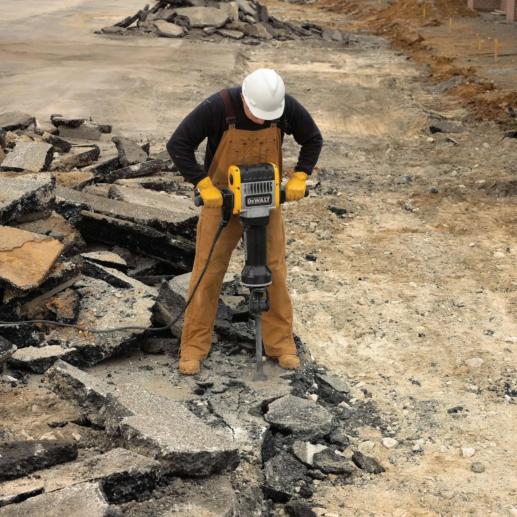Un trabajador con casco y guantes utiliza un martillo neumático DEWALT para romper concreto o asfalto en un sitio de construcción.