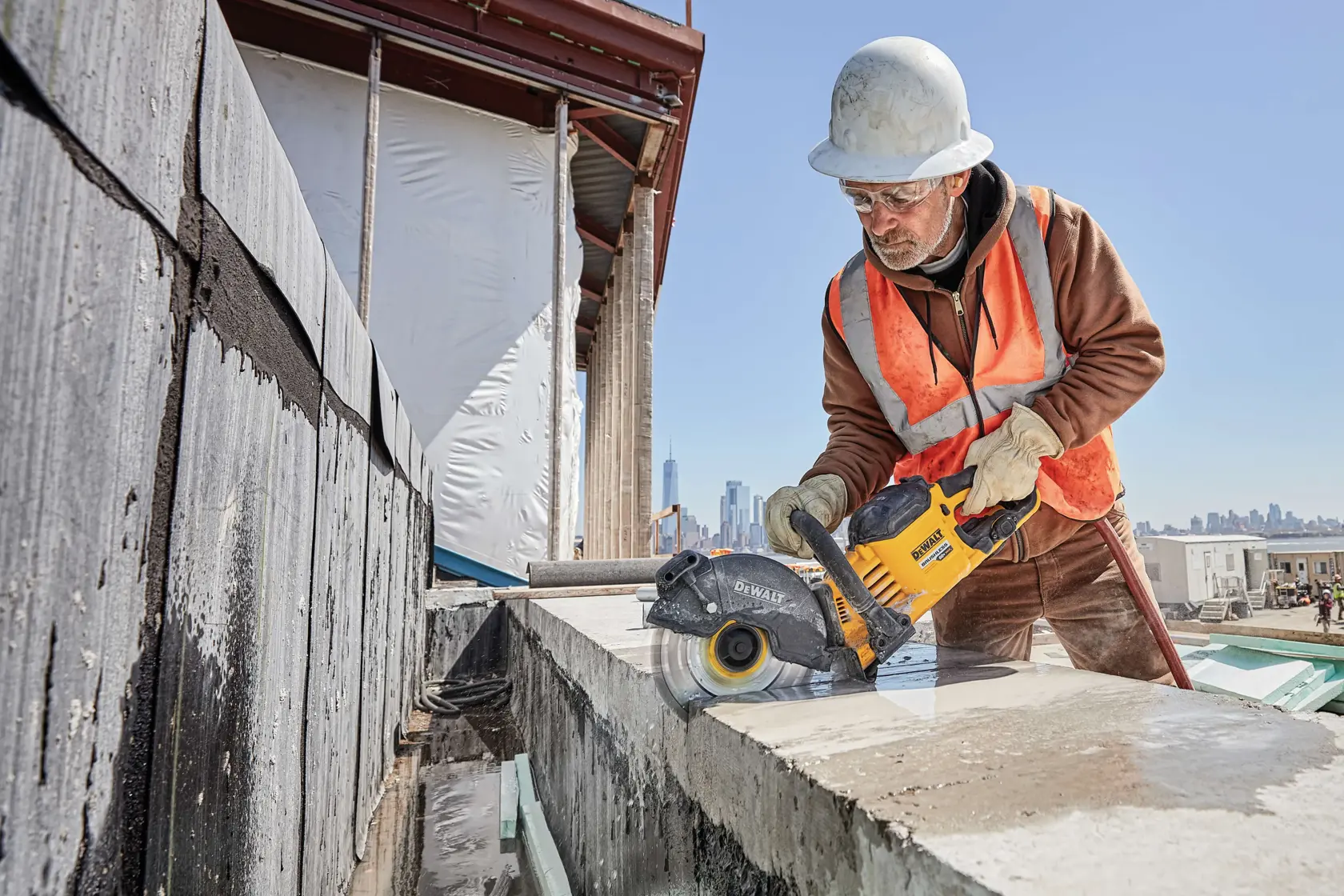 Trabajador usa herramienta DEWALT para cortar concreto en construcción, con casco y chaleco de seguridad.