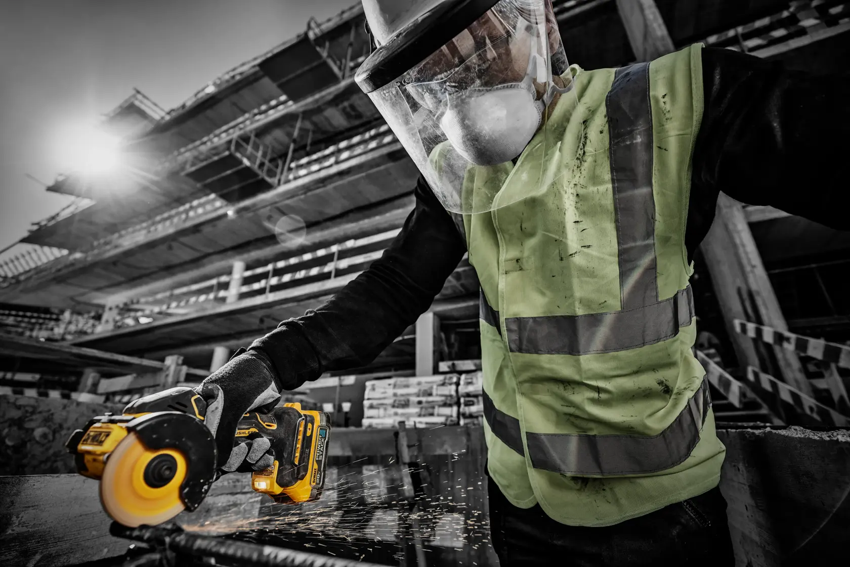 Una persona con chaleco de seguridad, mascarilla protectora y careta utiliza una herramienta inalámbrica DEWALT para cortar metal, mientras saltan chispas, en un sitio de construcción.
