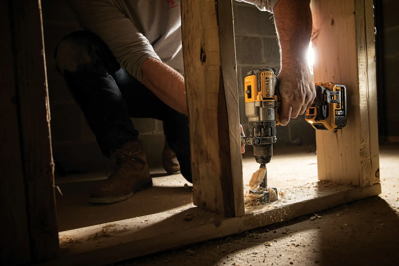 Una persona usando un taladro inalámbrico DEWALT (modelo DCD996P2) para perforar una viga de madera en un sitio de construcción.