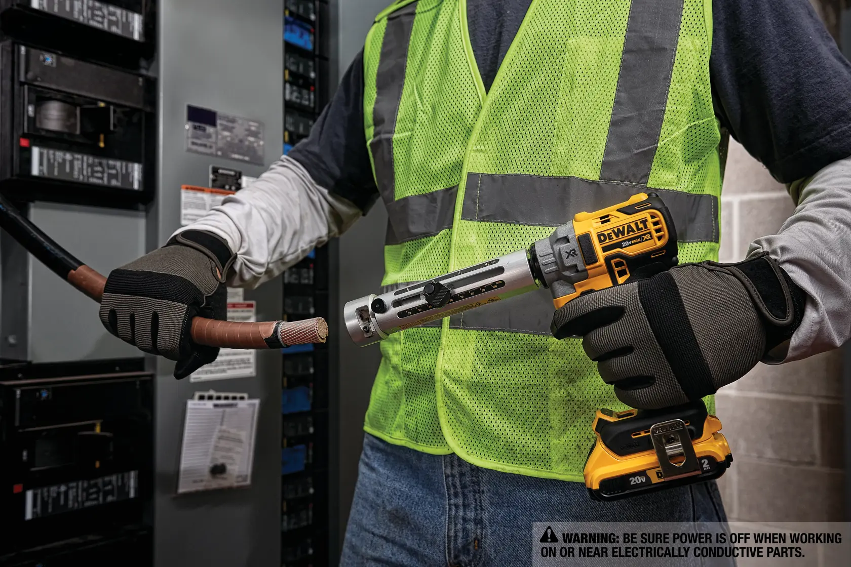 Uma pessoa usando luvas de segurança e colete refletivo utiliza uma ferramenta elétrica DEWALT para remover o isolamento de um cabo elétrico grosso em frente a um painel elétrico.