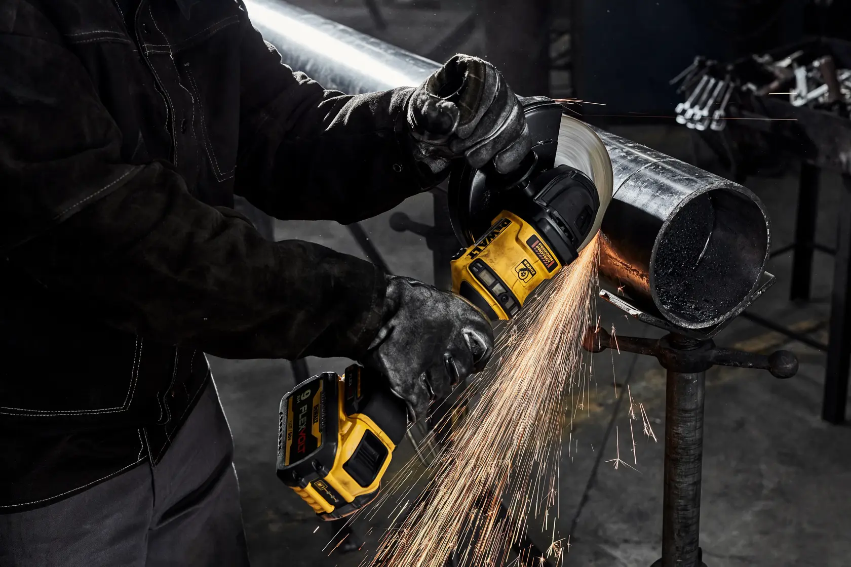 Un trabajador con guantes protectores utiliza una amoladora angular inalámbrica DEWALT para cortar una tubería de metal, produciendo chispas.