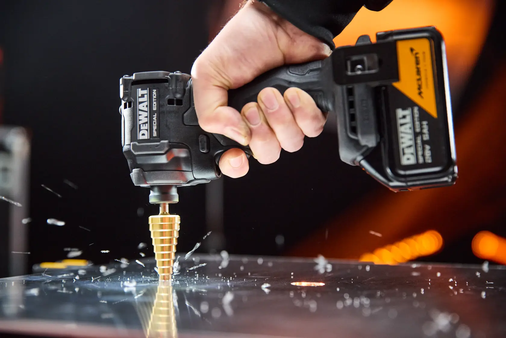 Mano usando taladro inalámbrico DEWALT con broca escalonada para cortar metal, causando virutas.