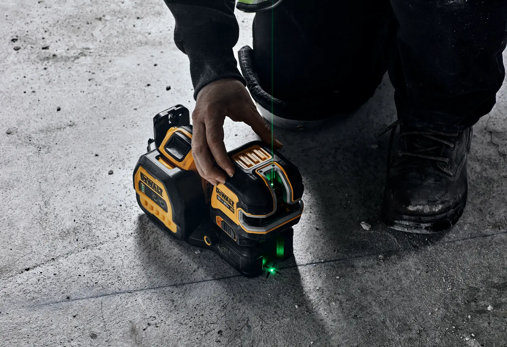 Primer plano de una persona usando una herramienta de nivel láser de línea verde DEWALT en un suelo de concreto. La herramienta proyecta una línea láser verde sobre la superficie para fines de alineación.
