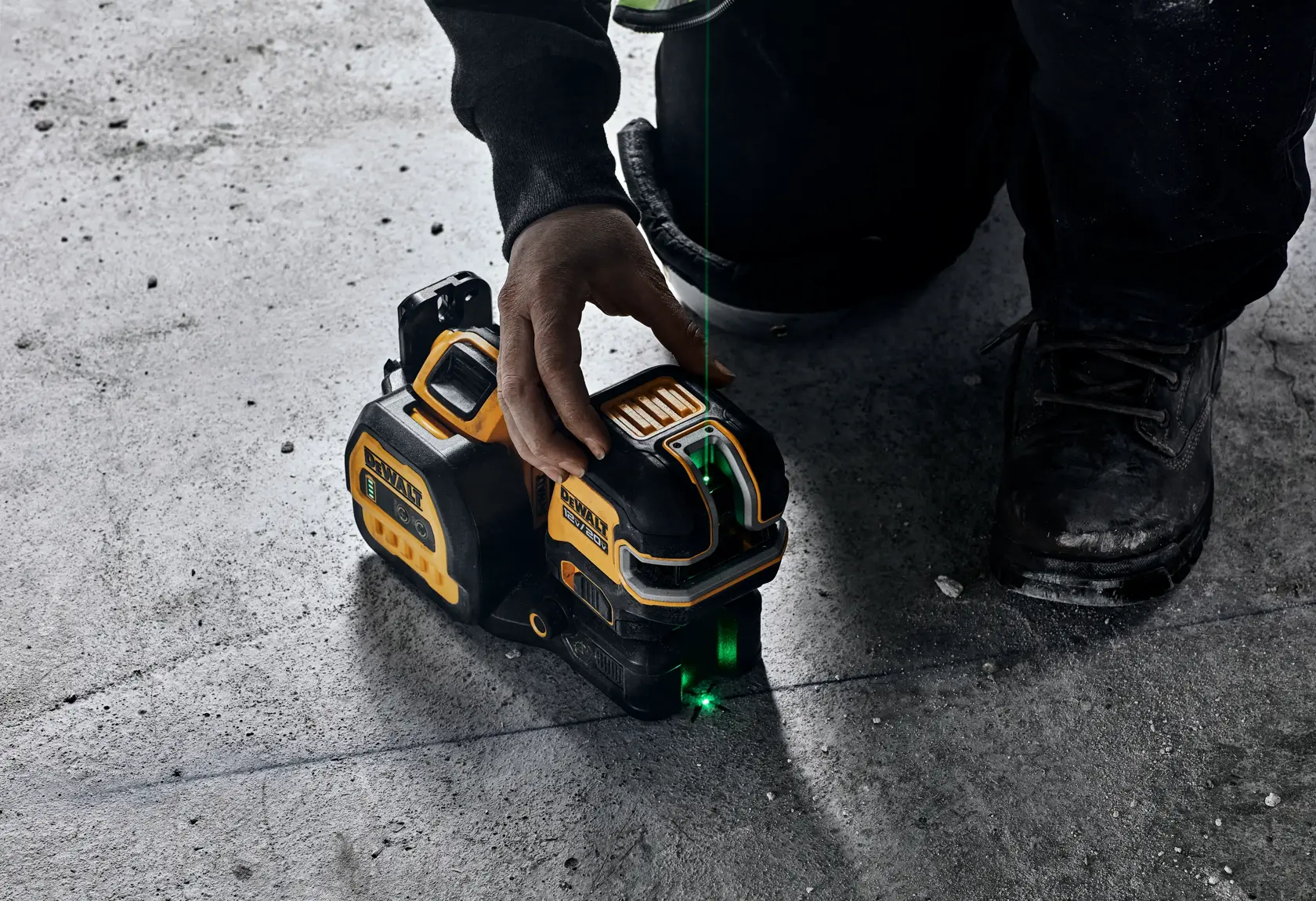 Una persona usando un nivel láser de línea verde DEWALT sobre un suelo de concreto. La herramienta proyecta una línea láser verde visible para una alineación precisa en tareas de construcción o medición.