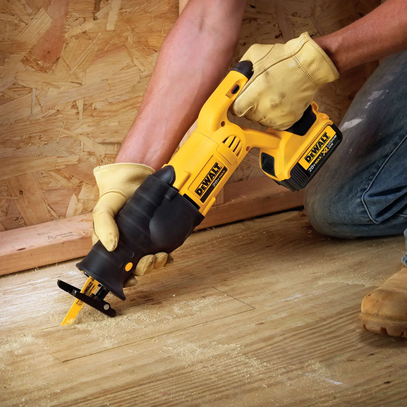 Una persona con guantes de trabajo utiliza una sierra recíproca inalámbrica DEWALT para cortar un suelo de madera. La sierra es amarilla y negra, y hay aserrín visible alrededor de la zona de corte.