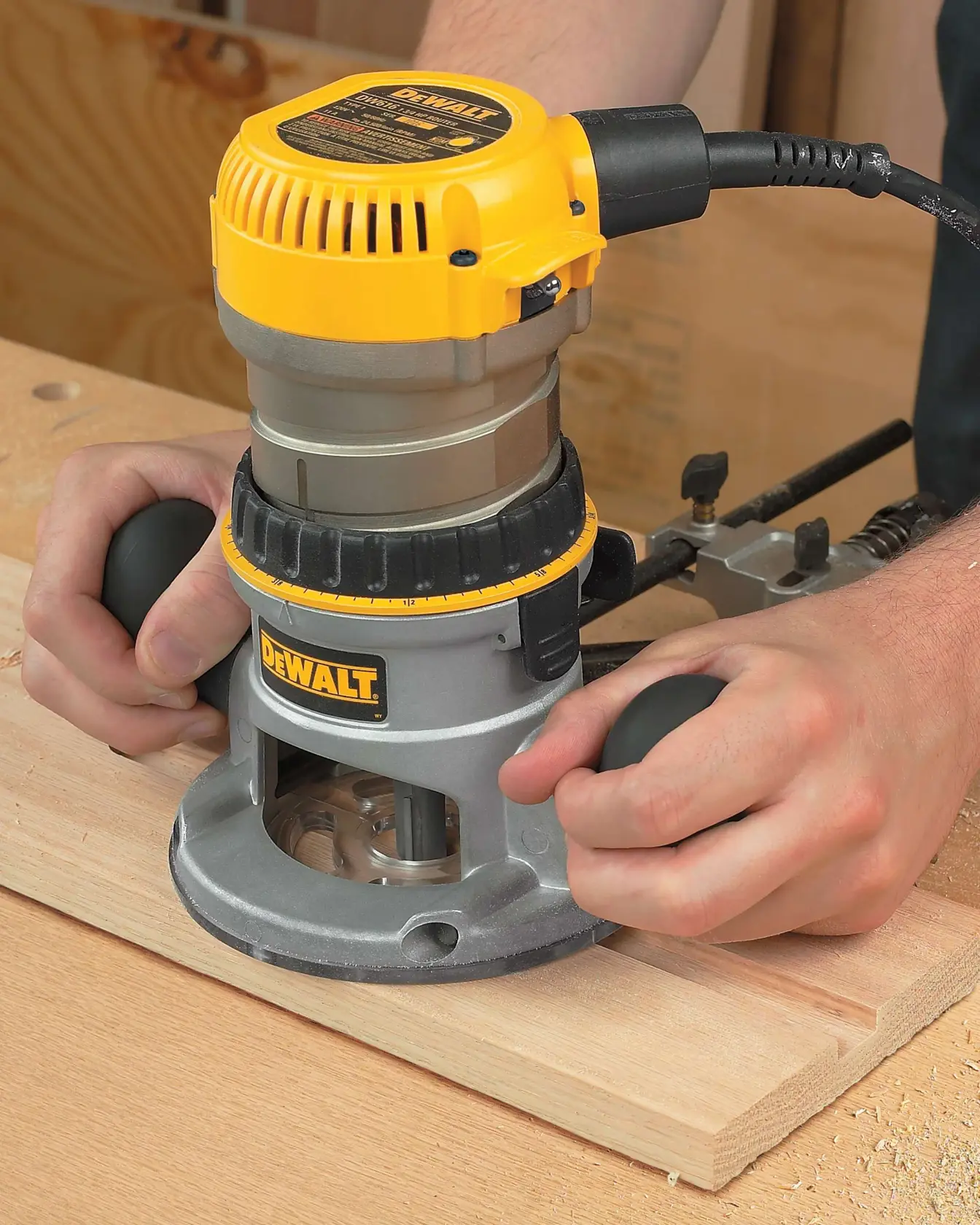 Primer plano de una persona usando una fresadora eléctrica DEWALT sobre una pieza de madera, mostrando ambas manos sujetando la herramienta.