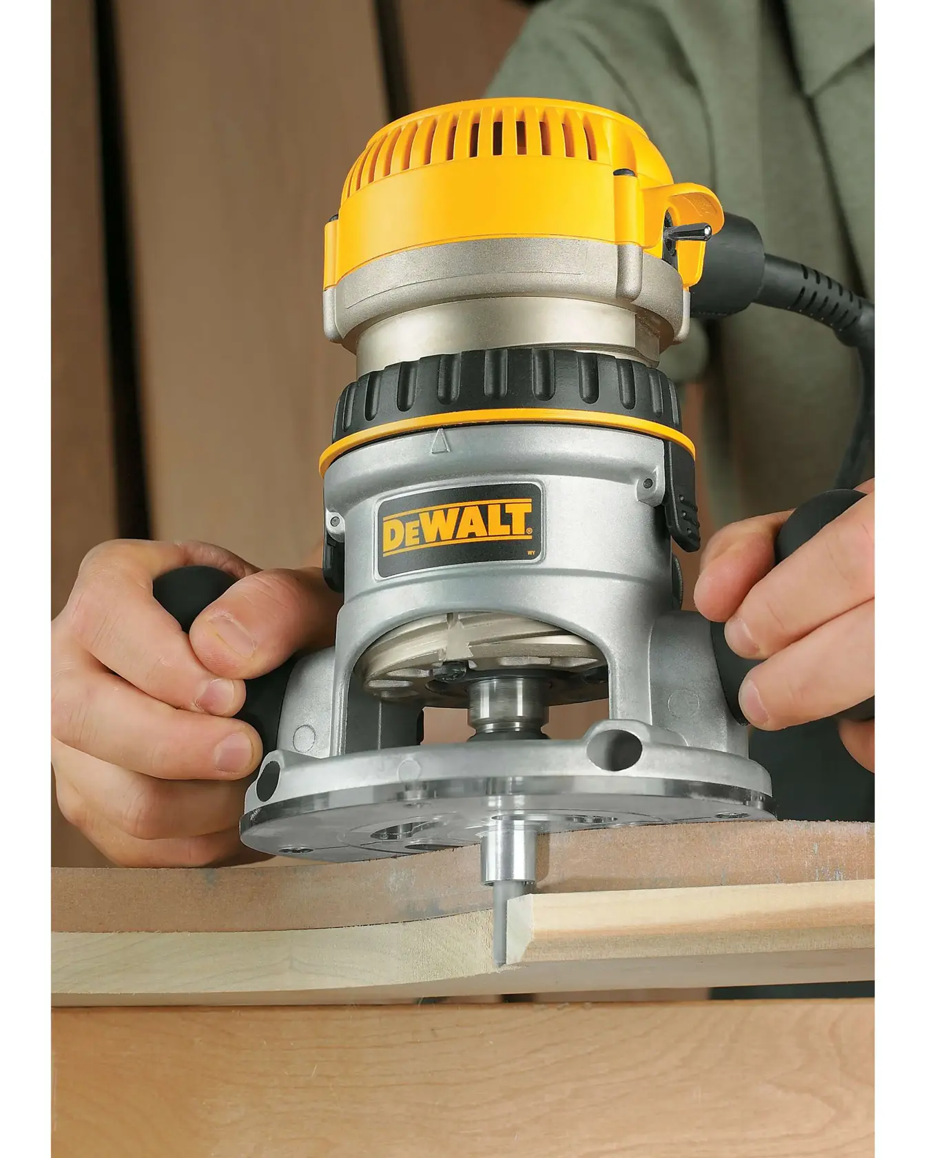 Vista de cerca de una fresadora para madera DEWALT DW616 que se utiliza para dar forma al borde de una pieza de madera. Las manos de una persona sujetan la herramienta y el logotipo de DEWALT es visible en el cuerpo de la fresadora.