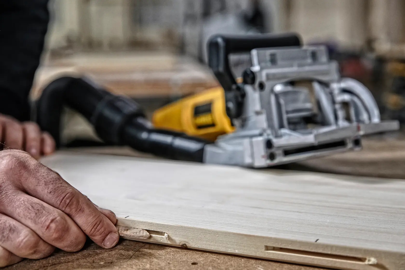 Primer plano de una herramienta de ensamblado DEWALT sobre una mesa de carpintería, con una persona insertando una galleta de madera en una ranura de una pieza de madera.