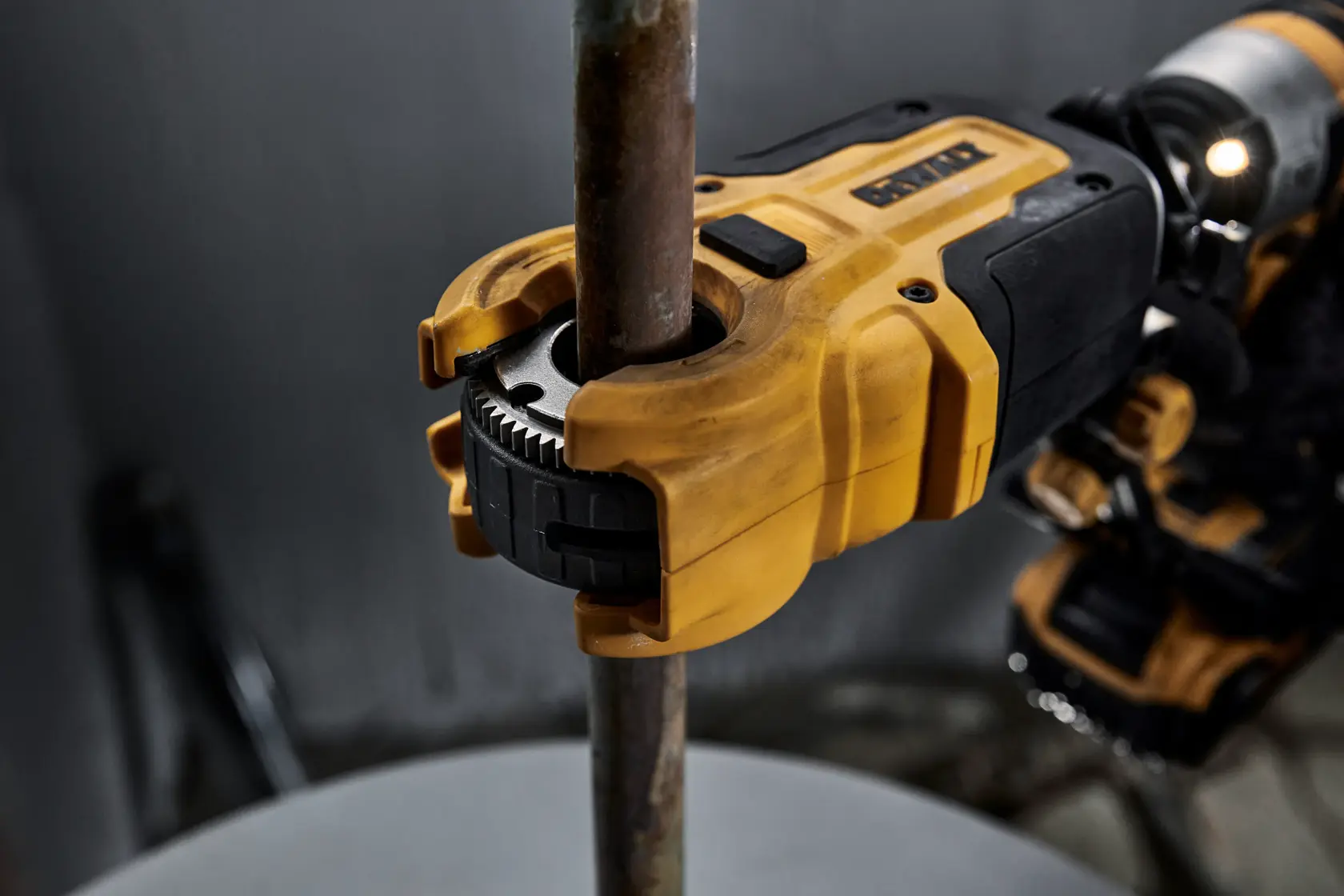 Primer plano de una herramienta eléctrica DEWALT utilizada para cortar o roscar un tubo metálico, mostrando la herramienta amarilla y negra sujetando firmemente el tubo.